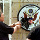 Two men remove the battered insignia from the gate of the US embassy in Beijing on May 12, 1999.